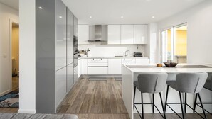 A modern kitchen with white cabinetry, a central island, and two bar stools. - Lagos Modern 1 With Pool by Homing (Lagos)