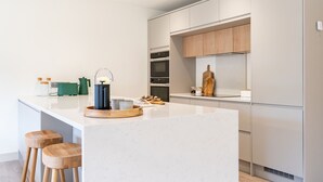 Une cuisine moderne avec un îlot central, des tabourets en bois et une bouilloire.
