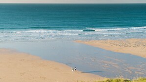 Une plage où deux personnes se promènent, un rivage sablonneux et l’océan.