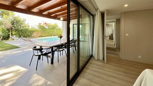 Un intérieur moderne avec un mur de verre donnant sur un espace piscine, un plafond en bois et un coin repas aménagé.