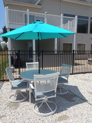 A patio with a round table and chairs, a turquoise umbrella, and a white fence. - Lake Anna Waterfront, Private Pool&Spa, Game Room, Pickle Ball, Tiki, Fire pit (Orange)