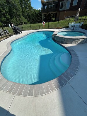 A swimming pool with a curved design, surrounded by a brick deck and a black metal fence. - Lake Anna Waterfront, Private Pool&Spa, Game Room, Pickle Ball, Tiki, Fire pit (Orange)