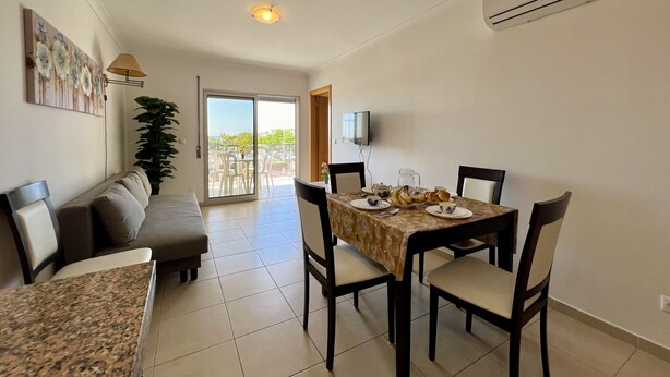 A dining area with a table set for four, a sofa, and a TV on the wall.