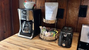Una cocina con cafetera, tostadora y un paquete de granos de café sobre la encimera.