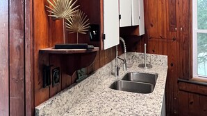 Una cocina con armarios de madera, encimera de granito, pileta de acero inoxidable y un espejo decorativo con diseño de sol.