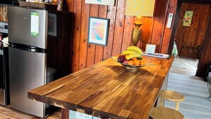 Una cocina con encimera de madera, un refrigerador, un microondas y un comedor con un taburete y una mesa.