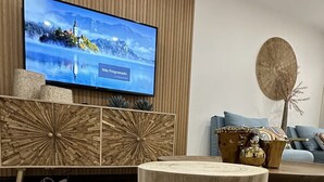 Ett vardagsrum med en tv monterad på en väggpanel av trä, ett runt soffbord i trä, en vävd pall och en mönstrad matta.
