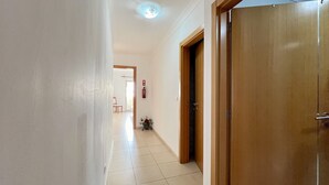 A hallway with a wooden door, a tiled floor, and a ceiling light fixture. - Monte Gordo Beach Ocean View 5 by Homing (Vila Real Santo Antonio)