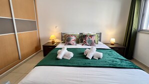 A hotel room with a bed, two nightstands, a green blanket, two pillows, and a window with curtains. - Monte Gordo Beach Ocean View 5 by Homing (Vila Real Santo Antonio)