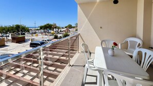 A balcony with a table and chairs, overlooking a parking area and a clear blue sky. - Monte Gordo Beach Ocean View 5 by Homing (Vila Real Santo Antonio)