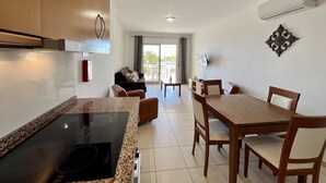 A modern kitchen with granite countertops, a built-in stove, and wooden cabinets. There is a dining area with a wooden table and chairs, and a living area with a sofa and a TV mounted on the wall. - Monte Gordo Beach Ocean View 5 by Homing (Vila Real Santo Antonio)
