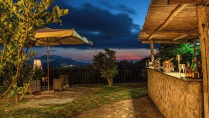 A patio area with a stone floor, a table with chairs, and a bar counter with bottles and glasses.