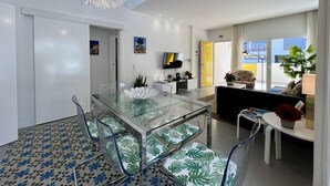 Un salon moderne avec une table à manger en verre, des chaises transparentes, un canapé et une grande fenêtre.