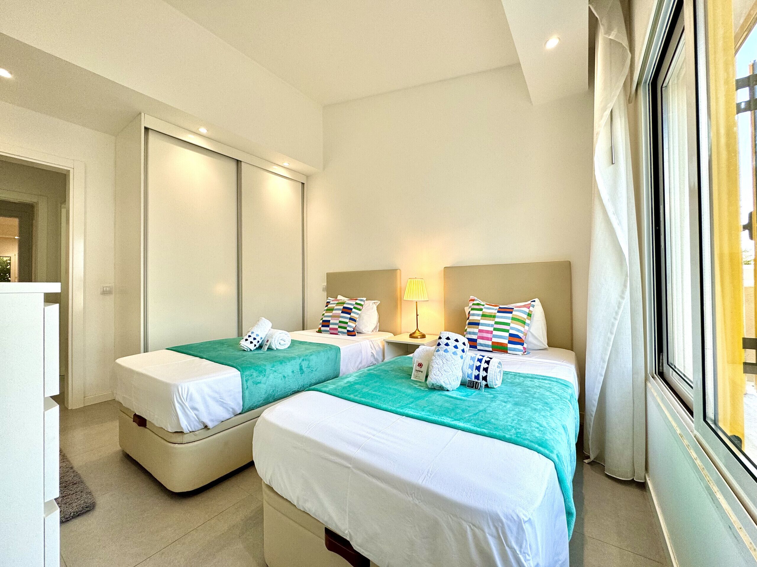 A hotel room with two beds, a desk, and a window.