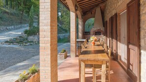 A covered outdoor dining area with a long wooden table and chairs, brick walls, and a stone fireplace. - Villa W/Infinty Pool Villa in the Heart of Chianti (Tregole)
