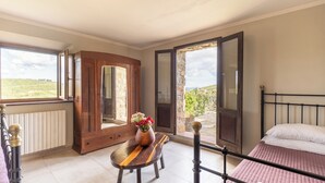 A bedroom with a bed, a wooden table with a vase of flowers, a view of the countryside through open doors, and a window with a view of the landscape. - Villa W/Infinty Pool Villa in the Heart of Chianti (Tregole)