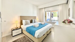 A modern bedroom with a large bed, bedside tables, a nightstand, and a view of the outdoors. - Vilamoura Club Villa 3 by Homing (Loulé)