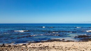 A beach with clear blue water, rocky shoreline, and distant mountains. - Kona Bali Kai#164 (Kailua-Kona)