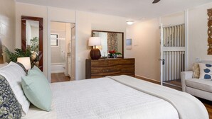A bedroom with a bed, a dresser, a mirror, a ceiling fan, and a door leading to a bathroom. - Kona Bali Kai#164 (Kailua-Kona)
