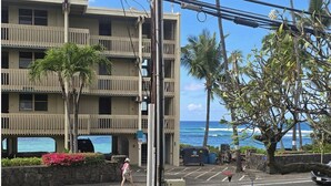 A multi-story building with balconies, a street with a pedestrian, and a view of the ocean. - Kona Bali Kai#164 (Kailua-Kona)