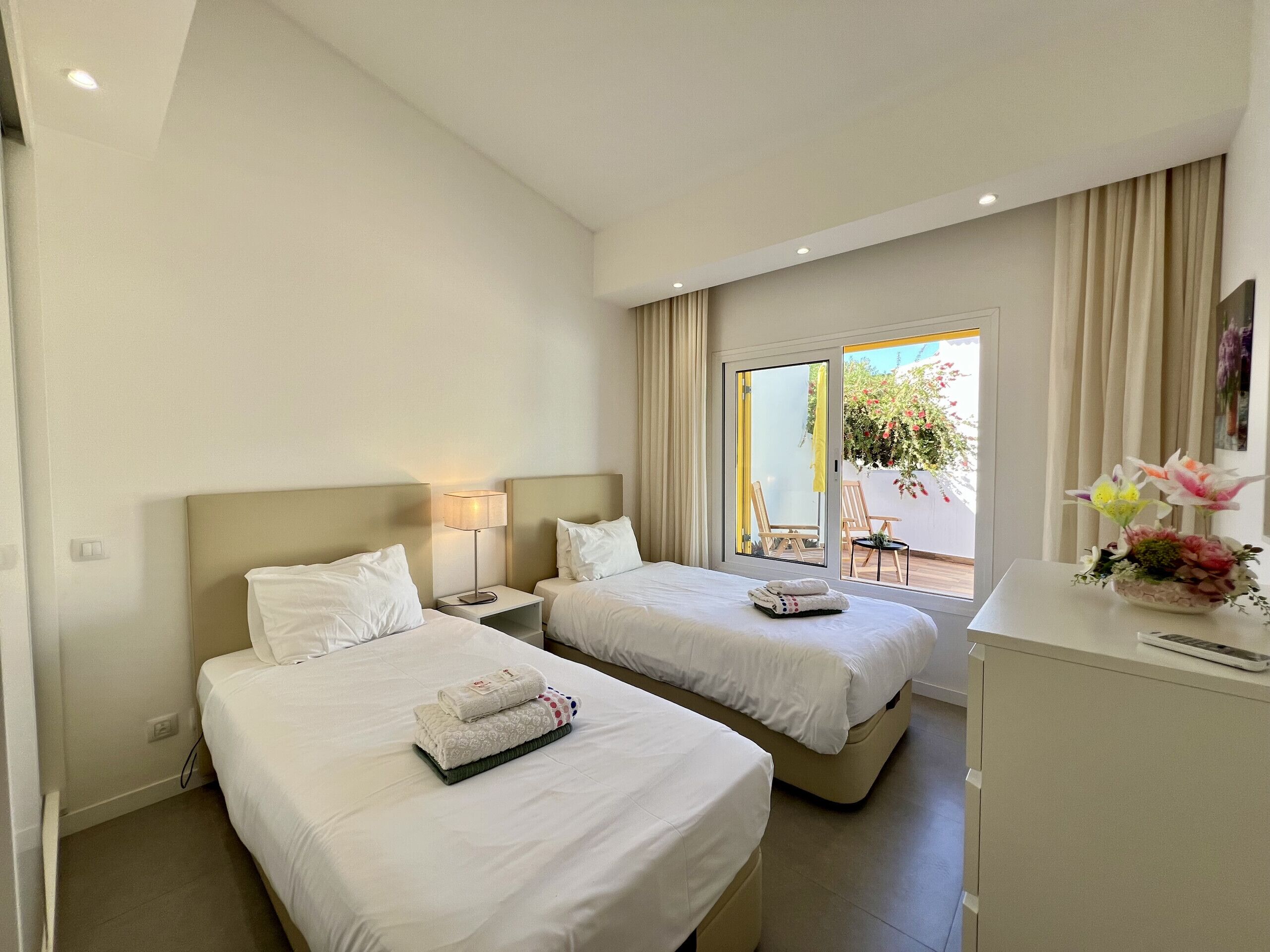 A hotel room with two beds, a desk, and a view of the outdoors.