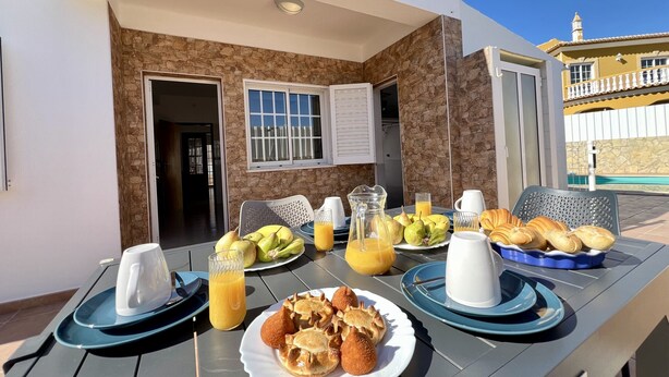 An outdoor dining area with a table set for breakfast, including fruits, pastries, and juice. - Pêra Stylish Villa With Pool by Homing (Silves)