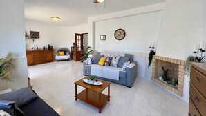 A spacious living room with a grey sofa, a wooden coffee table, and a ceiling fan. A fireplace with decorative plants is visible on the right. - Pêra Stylish Villa With Pool by Homing (Silves)