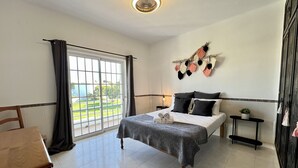 A hotel room with a bed, a desk, a chair, a nightstand, a potted plant, and a view of the outdoors. - Pêra Stylish Villa With Pool by Homing (Silves)