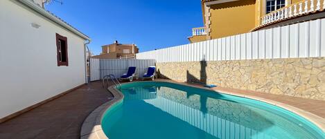 Una piscina con dos sillas de descanso, un muro de piedra y una cerca blanca.