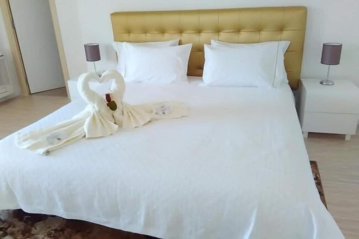 Una cama impecablemente hecha con un cabecero dorado, almohadas blancas y una toalla doblada en forma de cisne.
