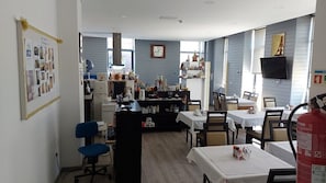 A dining area with tables and chairs, a kitchen area with appliances, and a bulletin board on the wall. - PALÁCIO NOVA  SEARA  2503 -AL (Armamar)