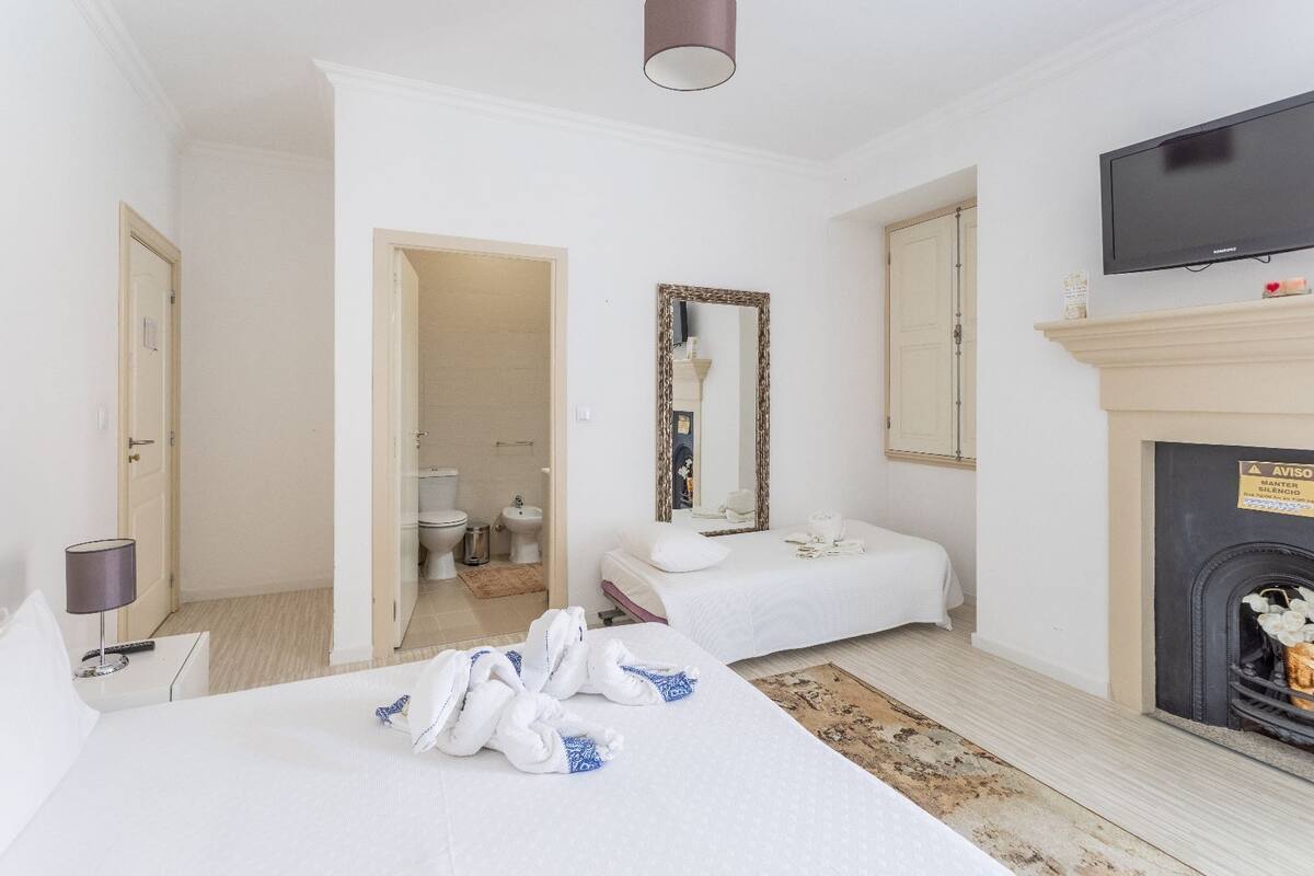 Habitación de hotel con cama, mesita de noche, lámpara, chimenea, televisión y un baño visible a través de una puerta abierta.