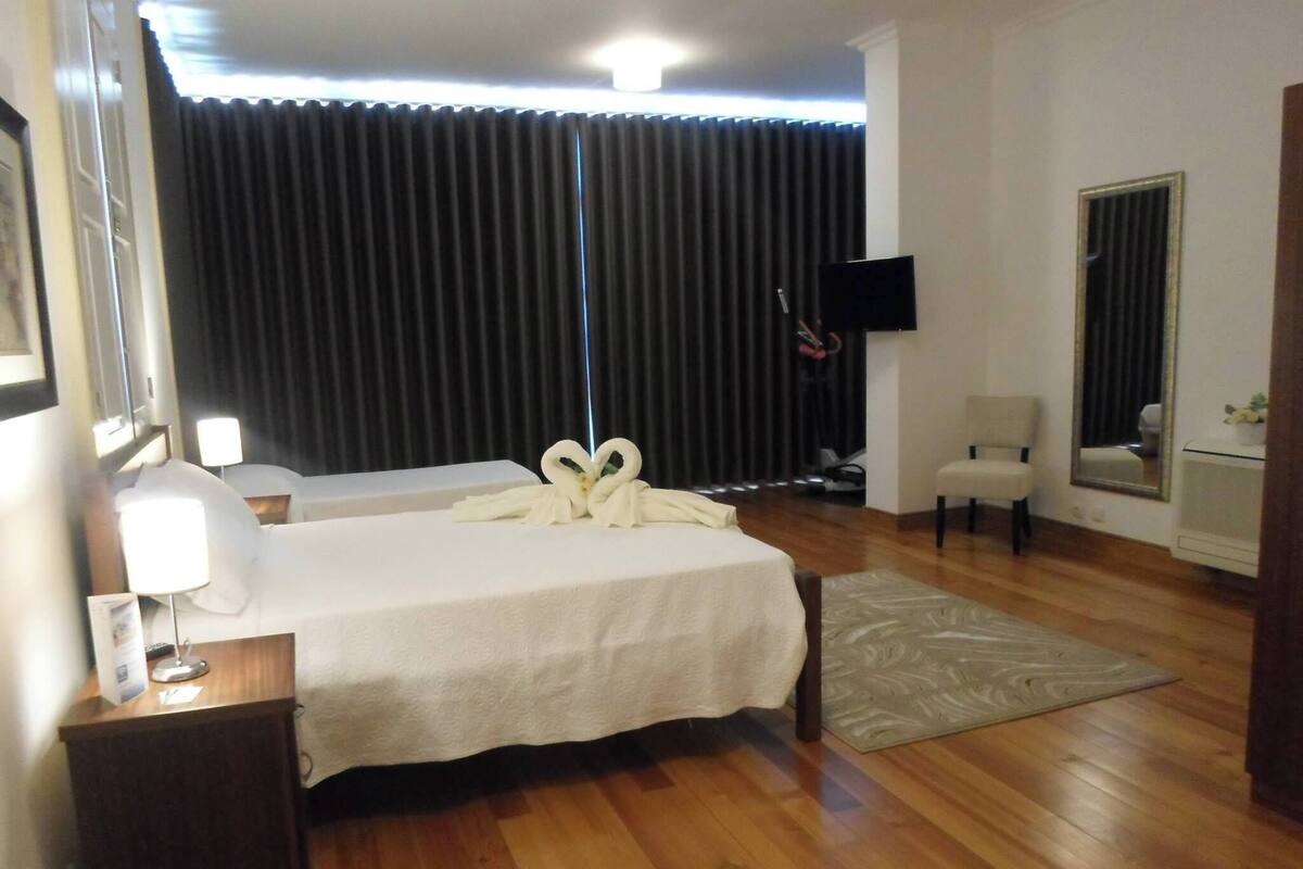 Habitación de hotel con una cama grande, un escritorio con lámpara, una silla, un televisor montado en la pared y un espejo.