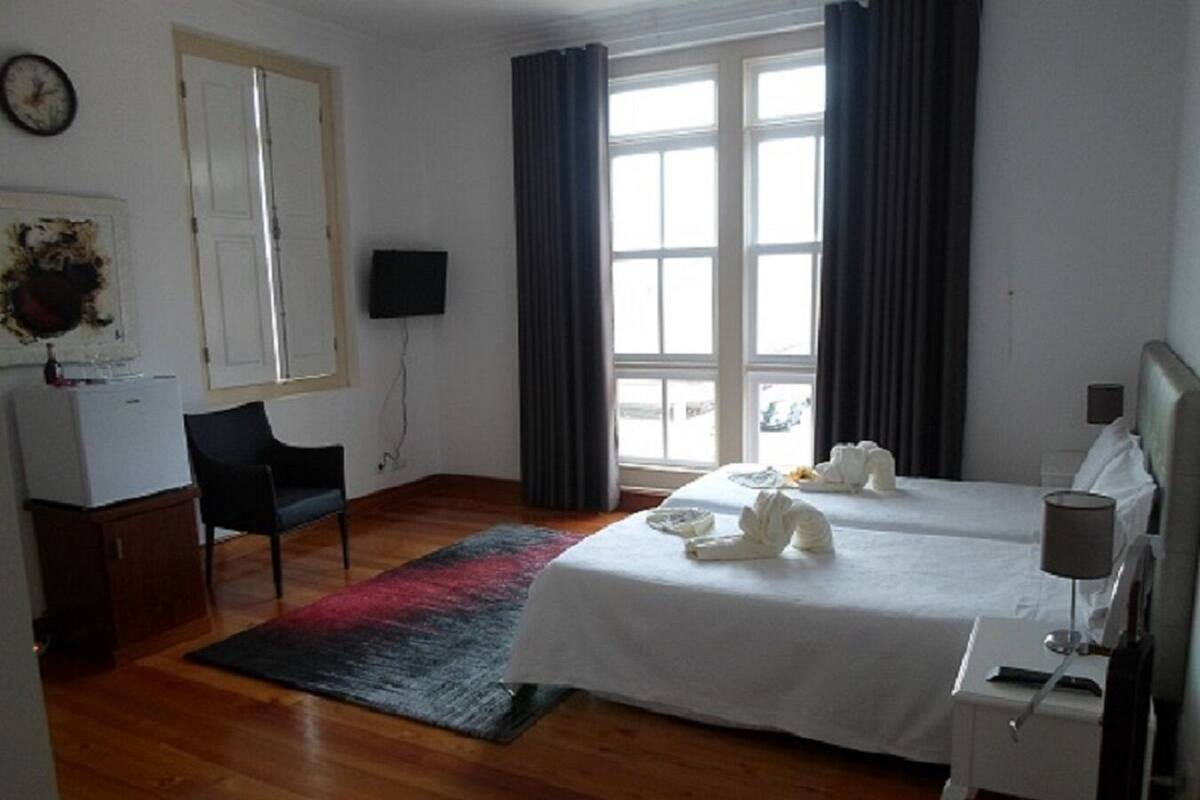Una habitación de hotel con cama, escritorio, silla, televisor y ventana con cortinas.