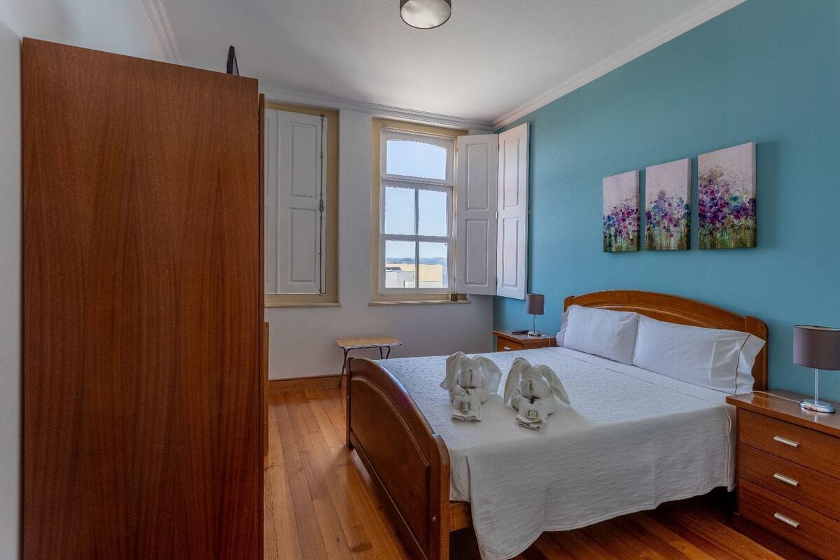 Un dormitorio con una cama de madera, una mesita de noche, un ventanal y tres cuadros florales en la pared.