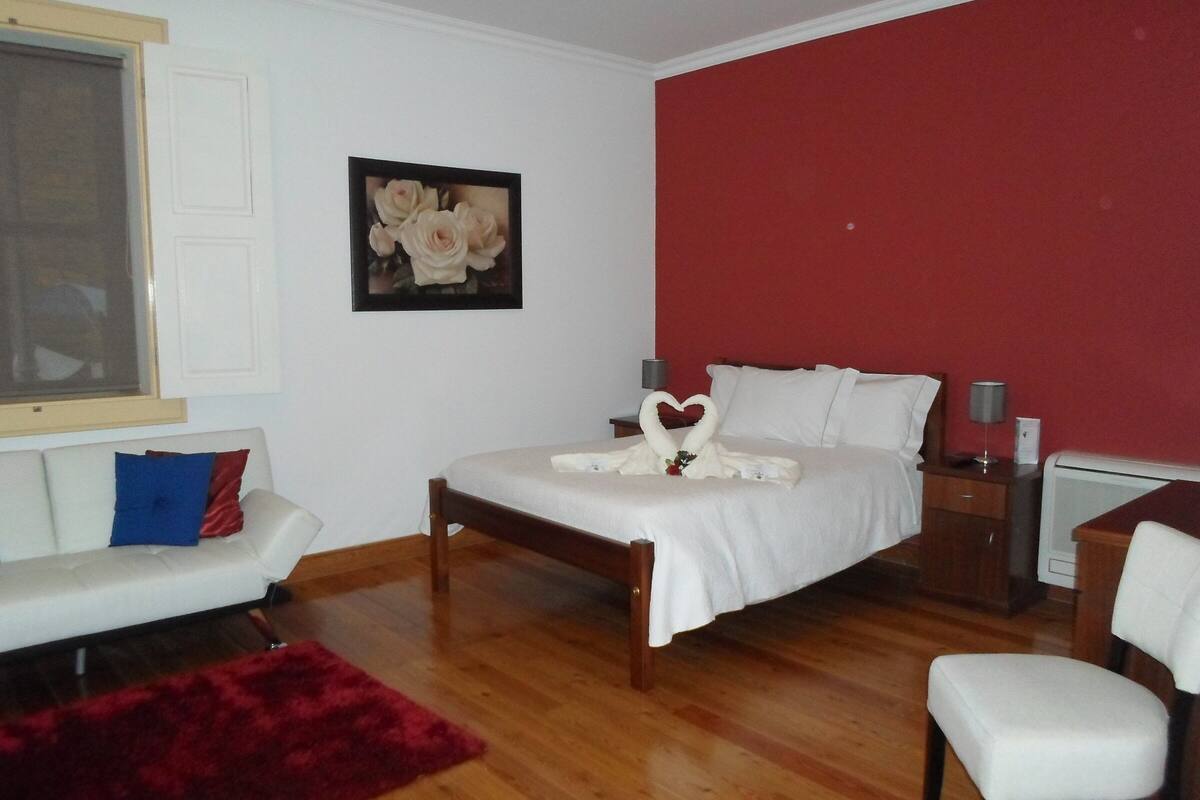 Un dormitorio con una cama, una mesita de noche, un escritorio, una silla, un tapete rojo y un cuadro de flores en la pared.