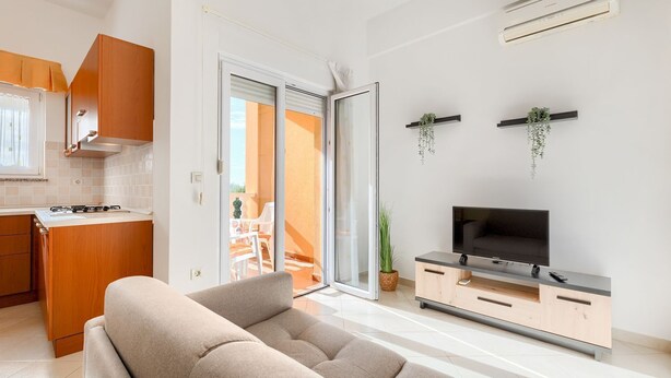 Ein modernes Wohnzimmer mit einer Couch, einem Fernseher auf einem Holzboden und einer Glastür, die auf einen Balkon führt.