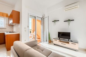 Una sala de estar moderna con un sofá, un televisor sobre un mueble de madera y un ventanal corredero que da a un balcón.