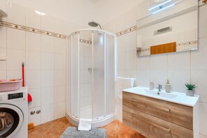 A modern bathroom with a glass-enclosed shower, a washing machine, and a wooden vanity with a sink.