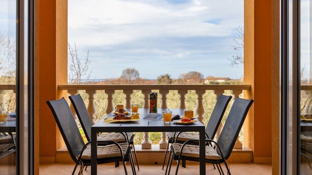 A balcony with a table set for breakfast, including pastries, juice, and coffee. - Affordable apartment with stylish interior, baby crib, playground (Vodnjan)
