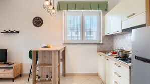 A compact kitchen with a wooden table, a built-in stove, and a window with curtains. - Affordable apartment with stylish interior, baby crib, playground (Vodnjan)