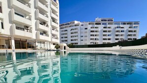 Una piscina con agua cristalina azul, rodeada de edificios blancos con balcones y ventanas.
