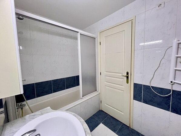 A bathroom with a bathtub, a white door, and a towel rack.