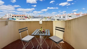 Un balcone con due sedie e un tavolo, vista su edifici e cielo sereno.