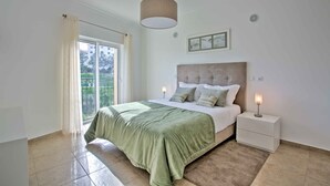 A bedroom with a bed, nightstands, a hanging light, a window with curtains, and a view of greenery outside. - Lagos Palm Tree 1 With Pool by Homing (Lagos)