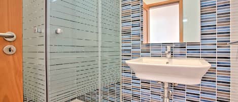 Un baño moderno con cabina de ducha de vidrio, un lavabo blanco y un espejo encima.