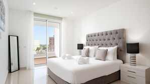A modern bedroom with a large bed, two bedside tables, a window with a view, and a door leading to an outdoor area. - Lagos Marina View 2 With Pool by Homing (Lagos)