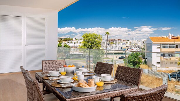 A balcony with a dining table set for breakfast, overlooking a marina and buildings. - Lagos Marina View 2 With Pool by Homing (Lagos)