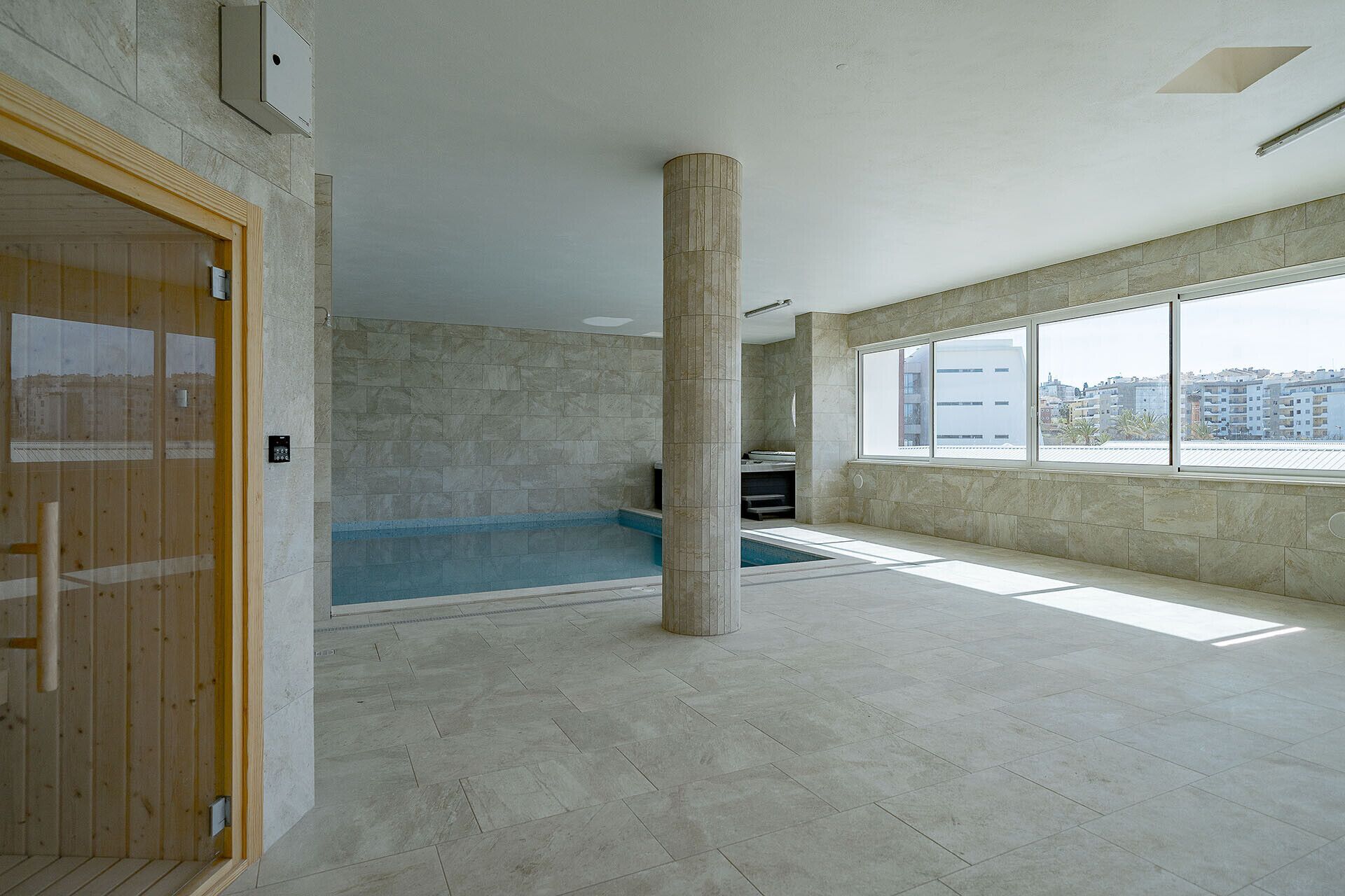 A spacious indoor swimming pool area with a large window providing a view of the cityscape.