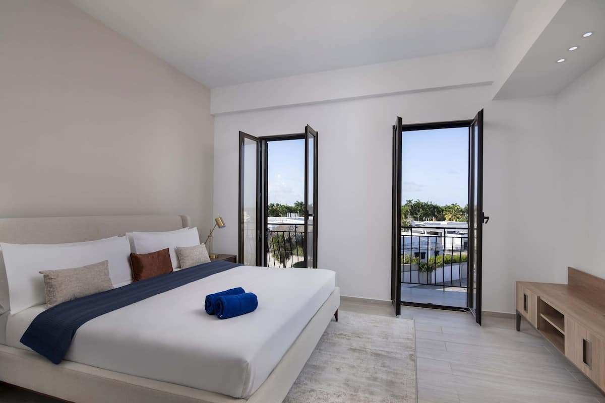 A modern bedroom with a large bed, a wooden bench, and a balcony with a view.